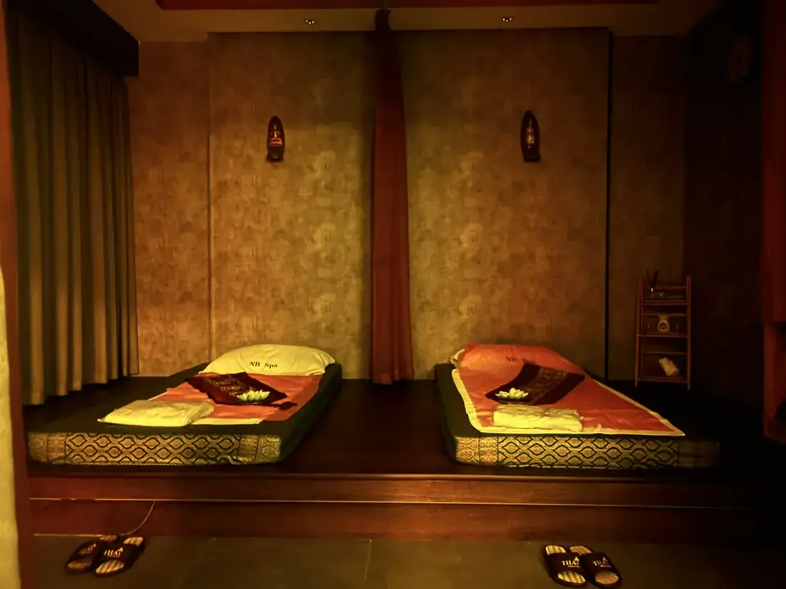 Couples Thai massage room with two floor mattresses side by side beneath carved wall shrines