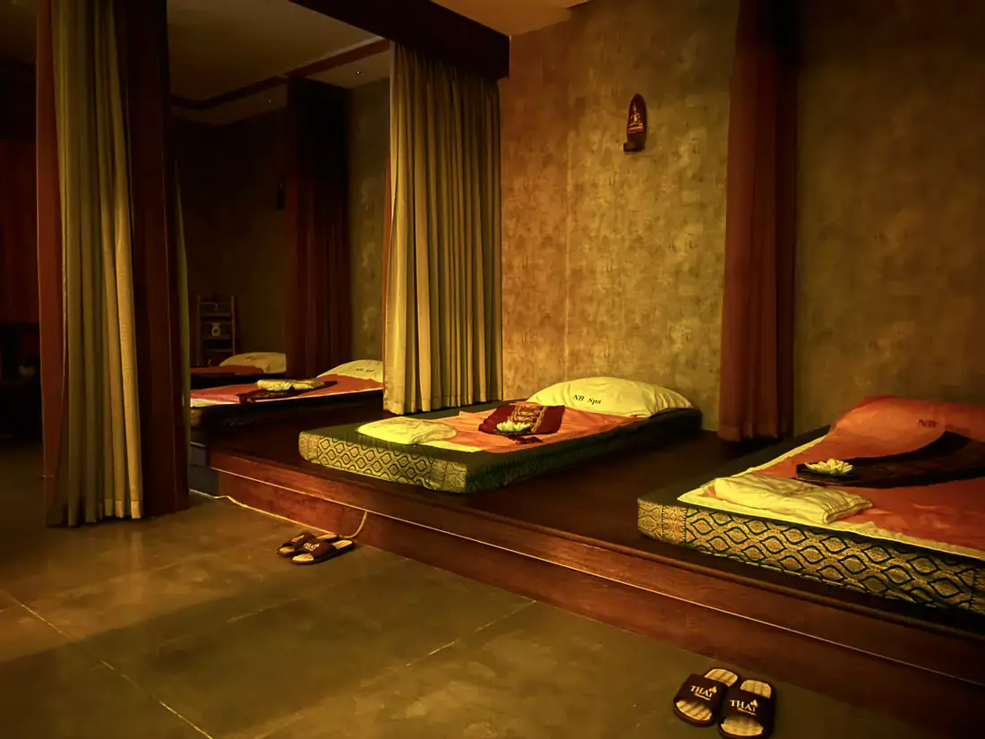 Traditional Thai massage mats on a raised wooden platform, each screened by curtains for privacy